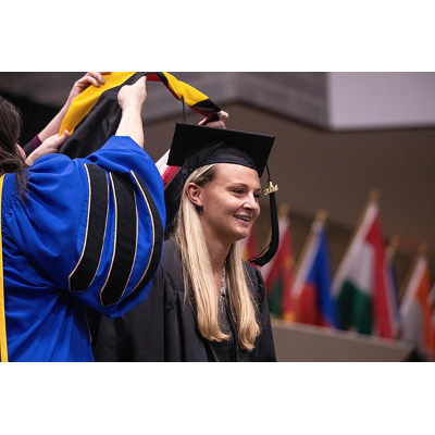 Platform party members assist a master's candidate in the formal hooding ceremony