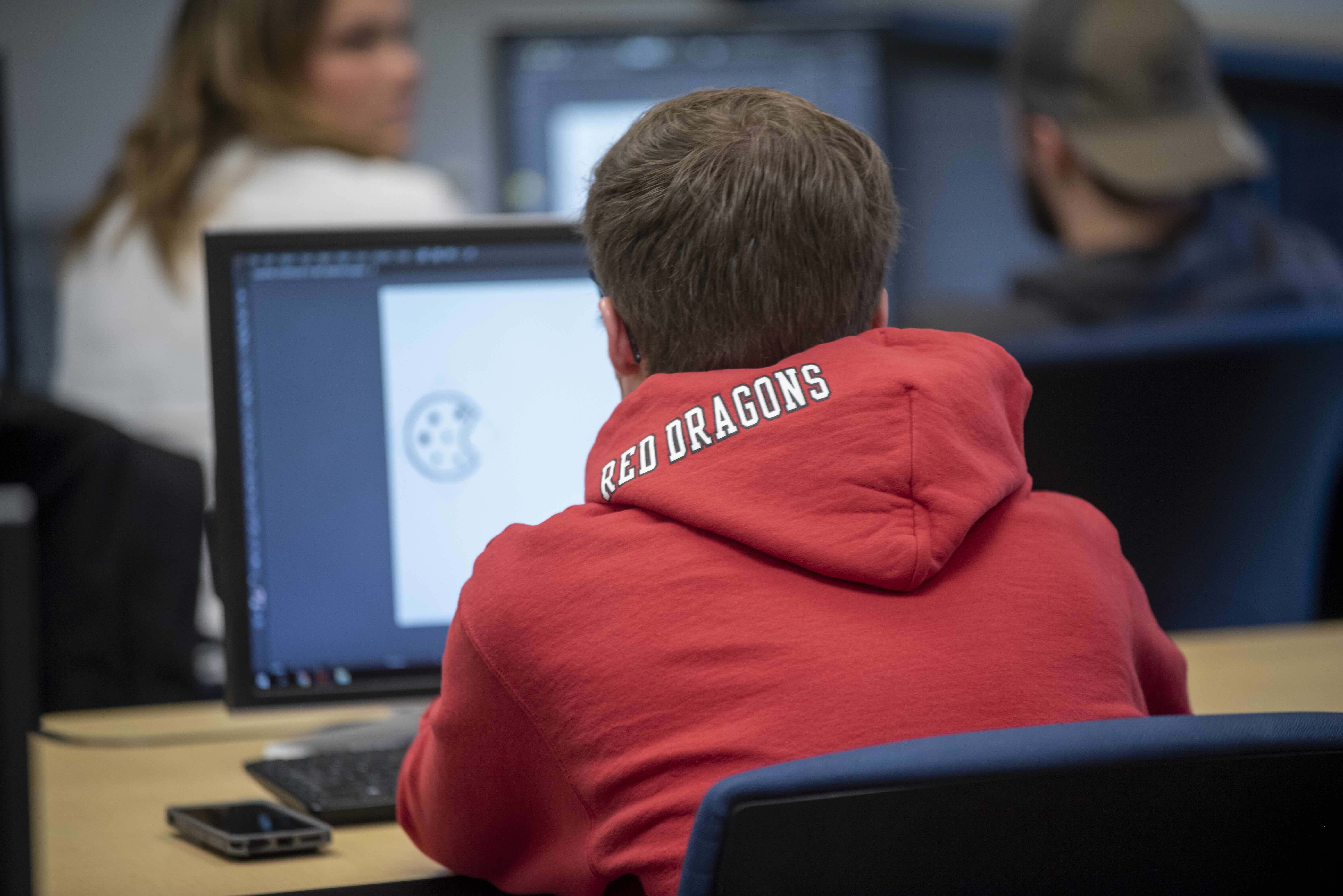 A student wearing a red dragon hoodie working at a compter