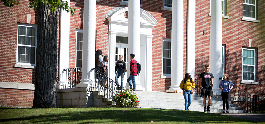 Cortland students in two groups chatting and walking outside of Brockway Hall