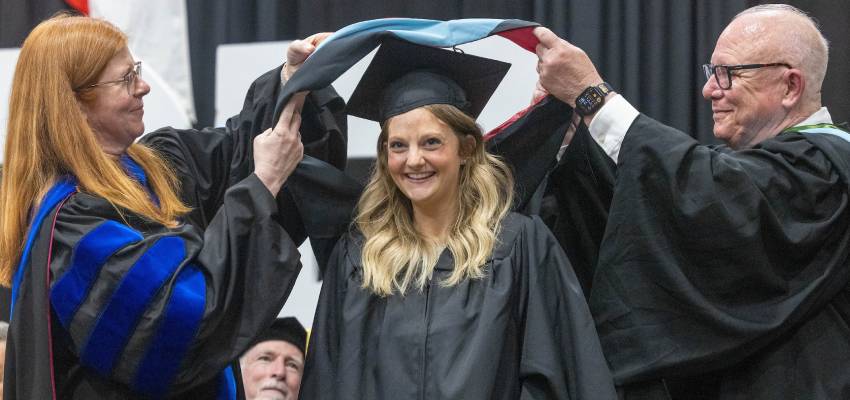 student smiling while being hooded at 2025 graduate commencement