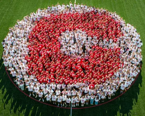 Students with white and red pose in the shape of a red C.